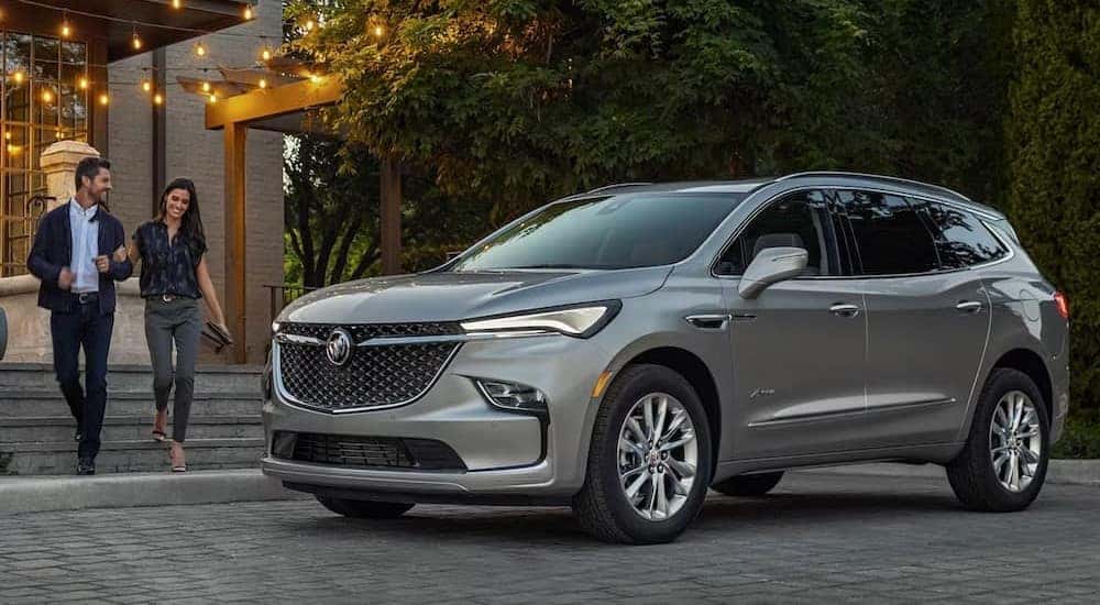 Two people are shown walking near a parked silver 2024 Buick Enclave Avenir.
