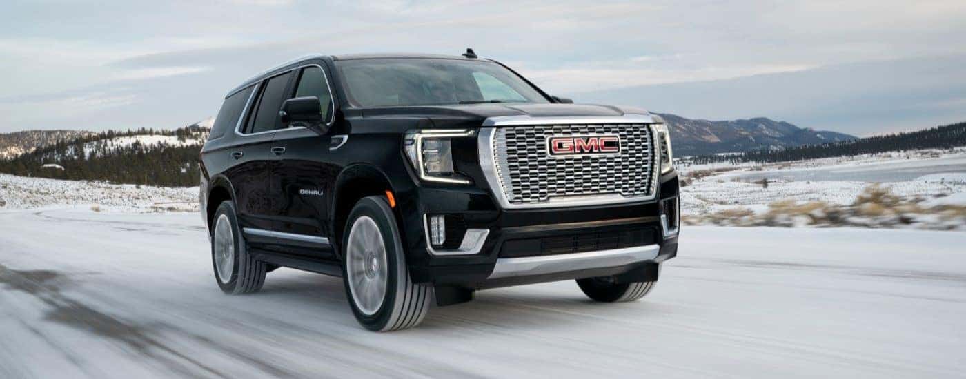 A black 2021 GMC Yukon Denali is shown driving on a snowy road.
