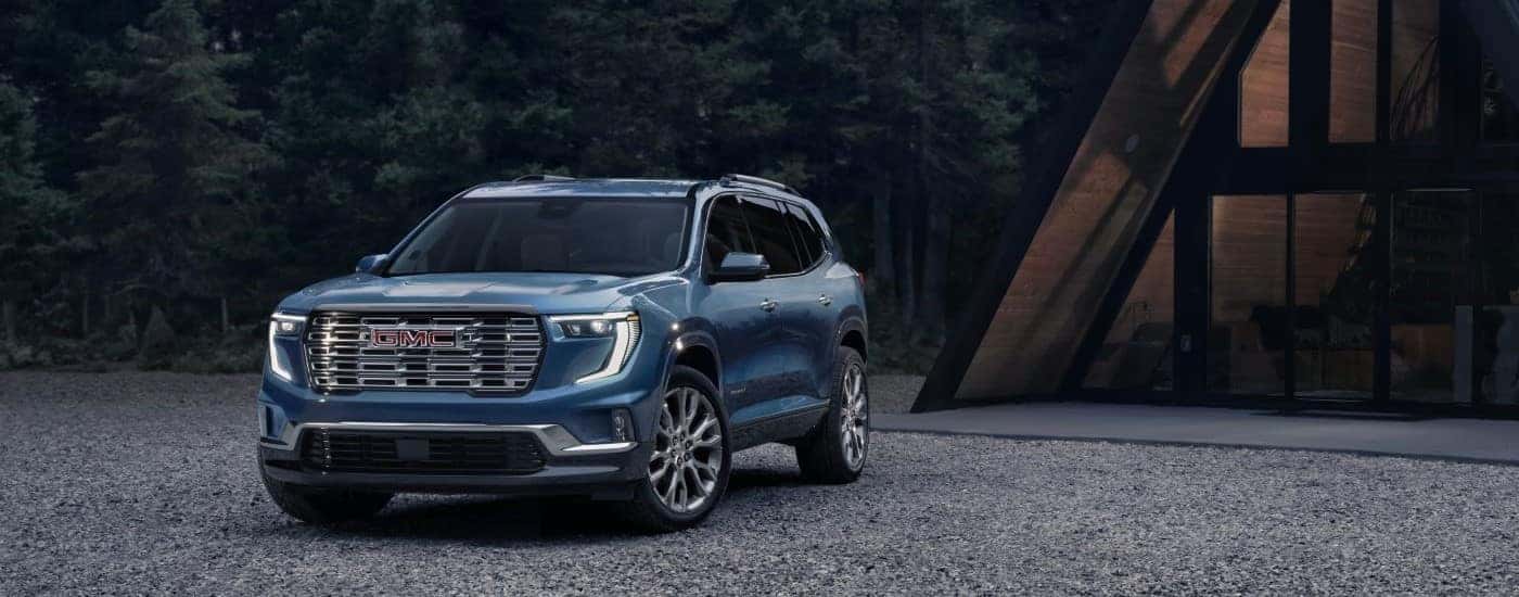 A blue 2024 GMC Acadia Denali is shown near a cabin after visiting a GMC dealer near Lombard.