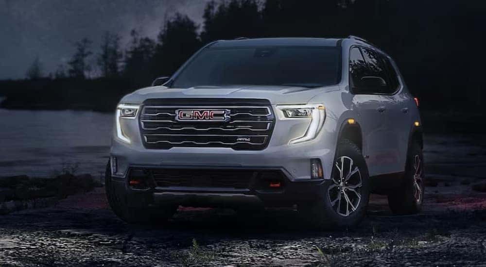 A popular GMC Acadia for sale, a white 2024 GMC Acadia AT4, is shown parked at night with the headlights on.