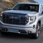 A silver 2024 GMC Sierra 1500 is shown driving on a highway after visiting an Aurora GMC dealer.