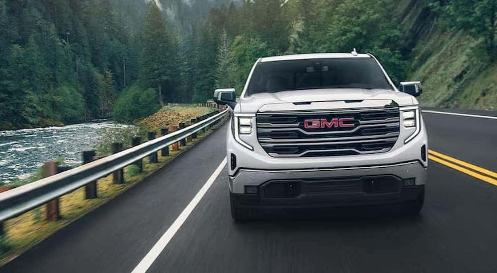 A white 2024 GMC Sierra 1500 Pro is shown driving on a highway near a river.