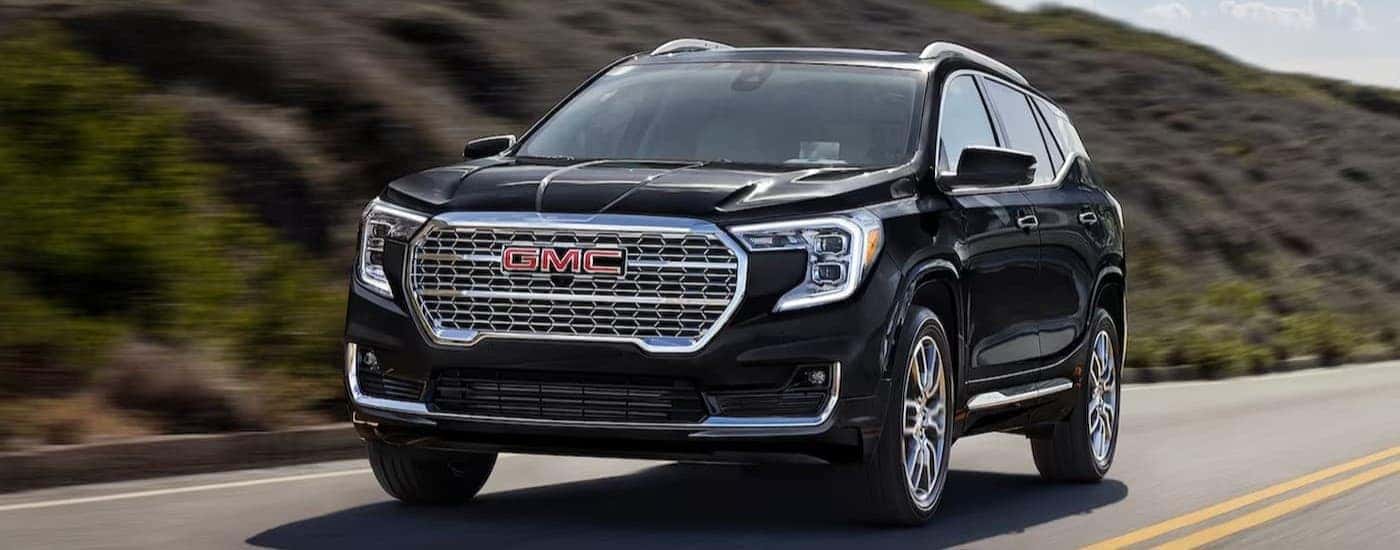 A black 2024 GMC Terrain is shown driving on a highway near a hill.