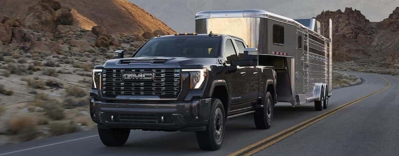 A black 2024 GMC Sierra 3500 HD is shown towing a trailer on a highway.