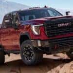 A red 2024 GMC Sierra 2500 AT4X HD off-roading over rocks.
