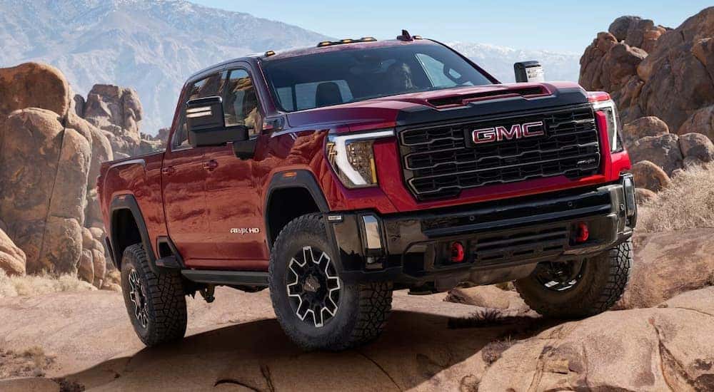 A red 2024 GMC Sierra 2500 AT4X HD off-roading over rocks.