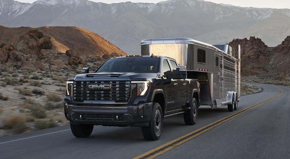 A black 2024 GMC Sierra 2500 Denali HD towing a large trailer on the highway.