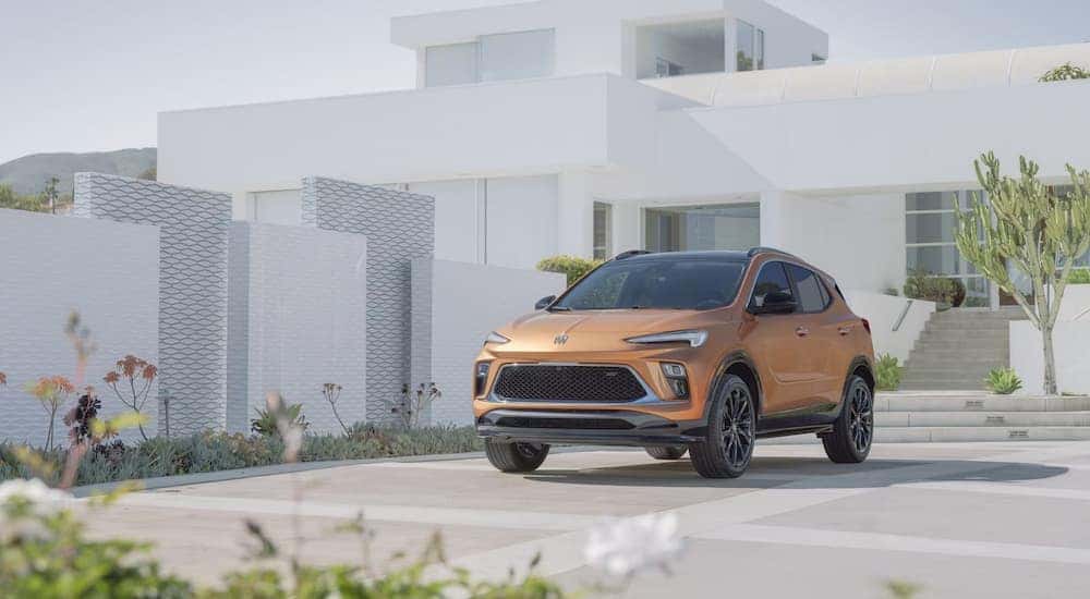 A gold 2024 Buick Encore GX Sport Touring parked outside a modern home.