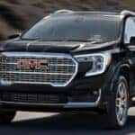 A black 2024 GMC Terrain for sale is shown driving on a highway.
