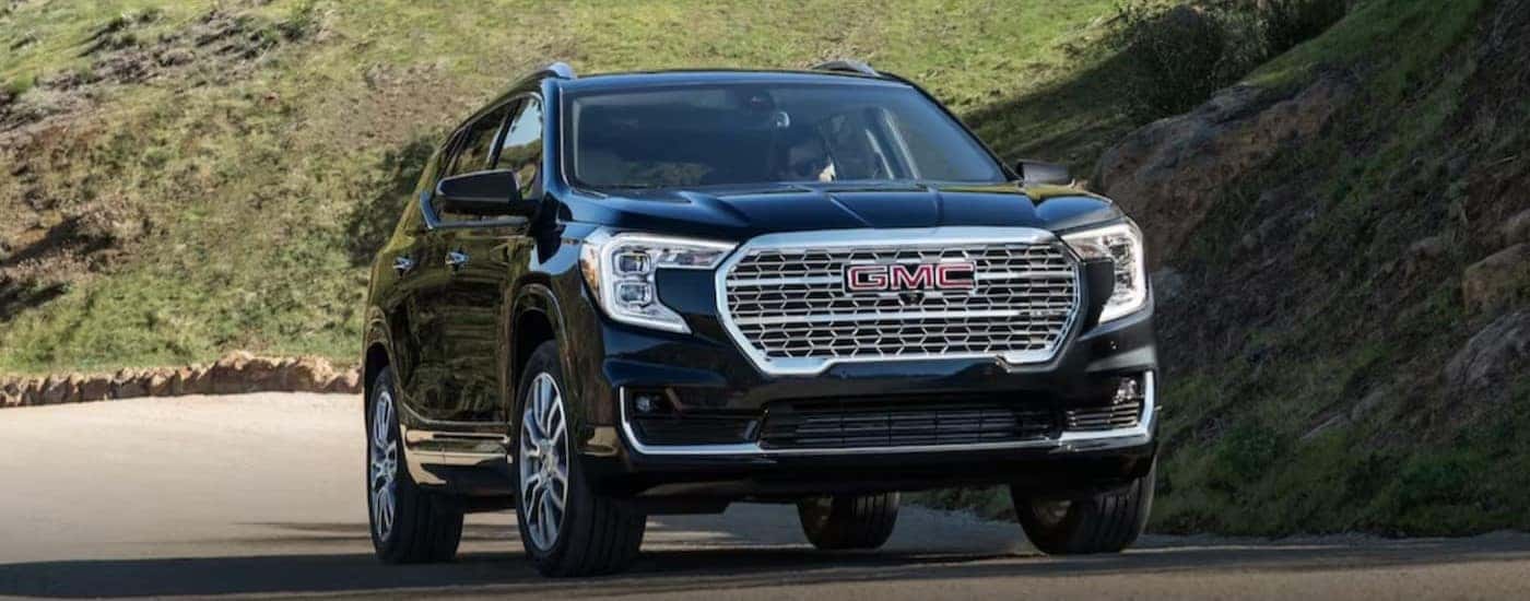 A black 2024 GMC Terrain is shown driving up a hill.