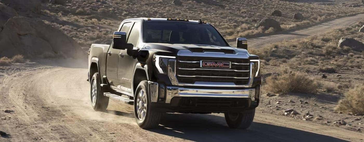 A black 2024 GMC Sierra 2500HD is shown driving off-road.