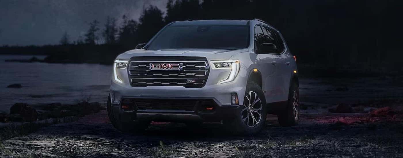A silver 2024 GMC Acadia AT4 is shown parked near a lake.