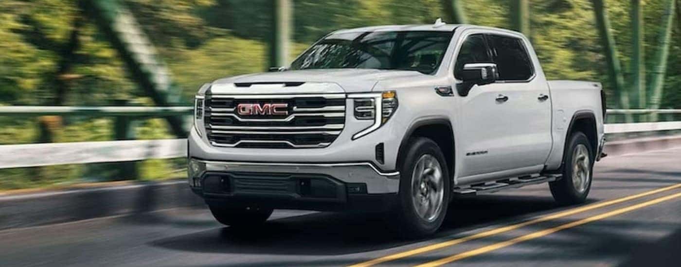 A white 2024 GMC Sierra 1500 SLE is shown driving to visit a GMC dealer.