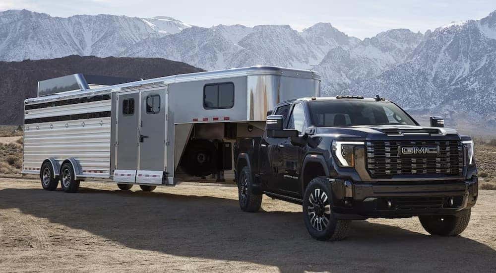 A black 2024 GMC Sierra 3500 HD Denali is shown towing a trailer.