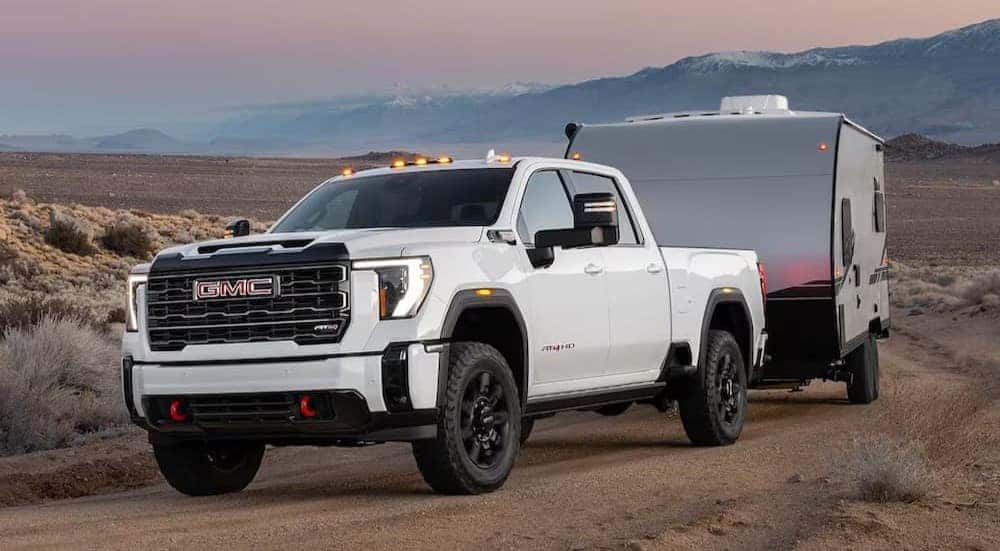 A white 2025 GMC Sierra 1500 HD AT4 is shown towing a trailer after visiting a Buick GMC dealer near Naperville.