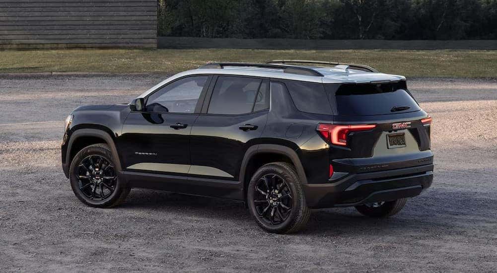 A black 2025 GMC Terrain is shown parked near a wooden building.