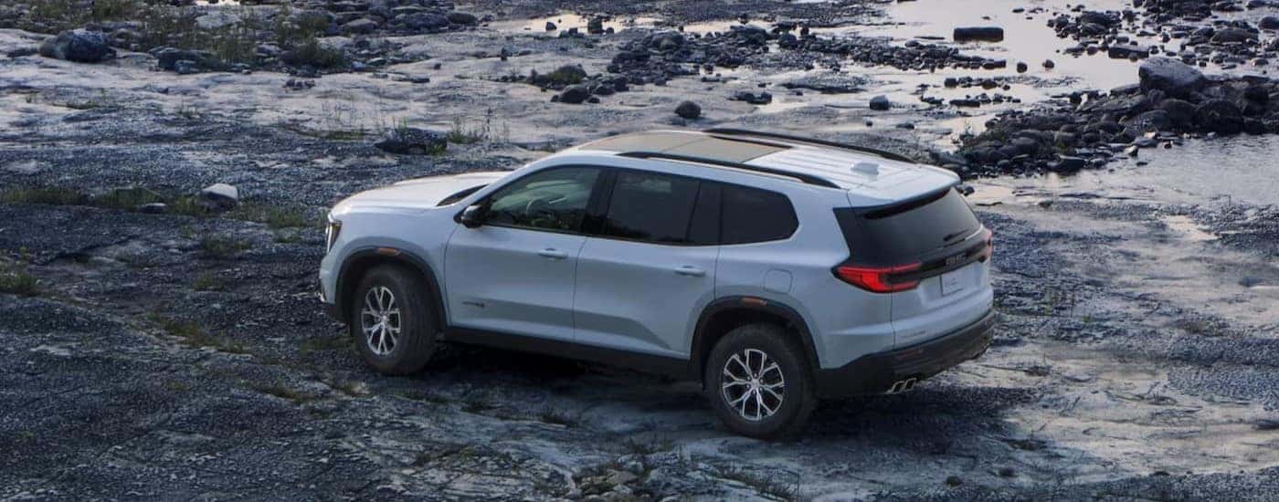 A white 2024 GMC Acadia AT4 is shown parked off-road.