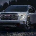 Left angled view of a white 2025 GMC Acadia Denali parked on a beach.