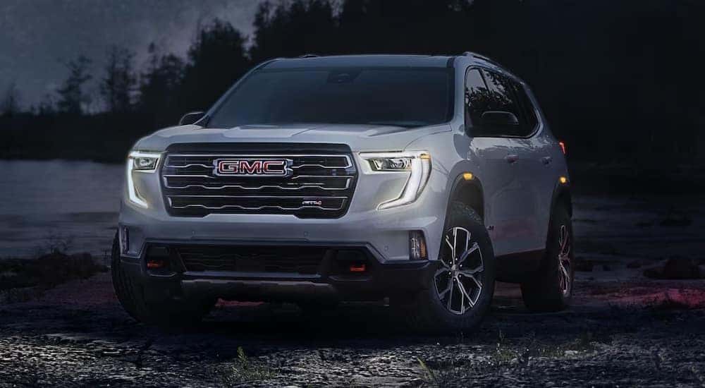 Left angled view of a white 2025 GMC Acadia AT4 parked on a beach.