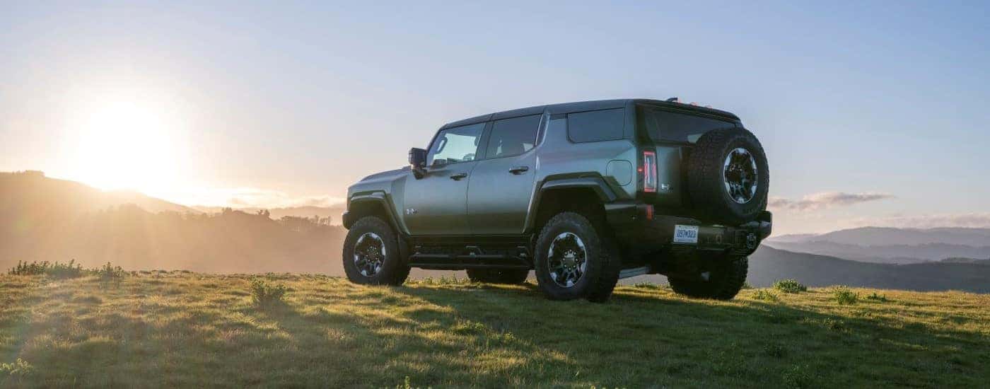 Rear view of a green 2024 GMC Hummer EV parked off-road.