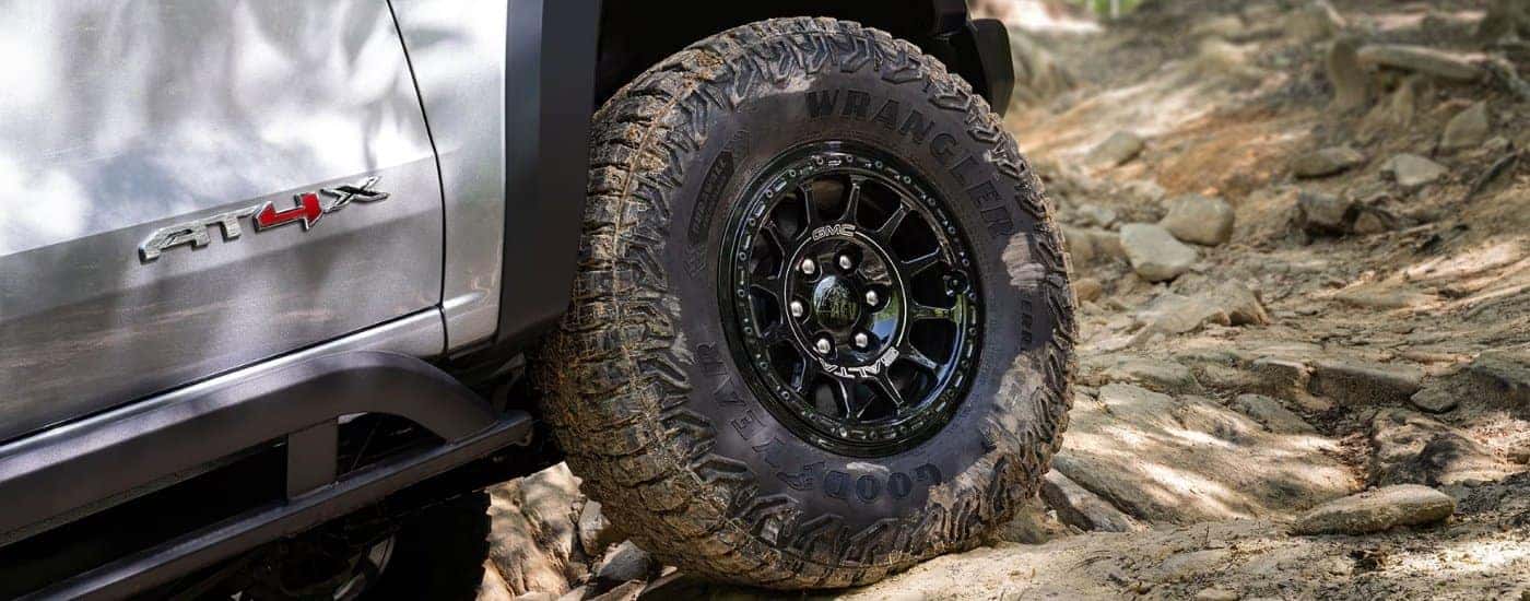 A close-up shows a black wheel on a white 2025 GMC Canyon AT4X.