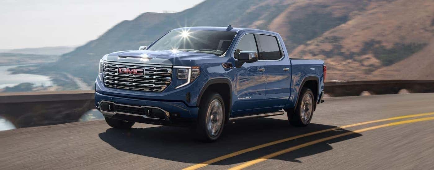 A blue 2024 GMC Sierra 1500 is shown driving to a car dealer.