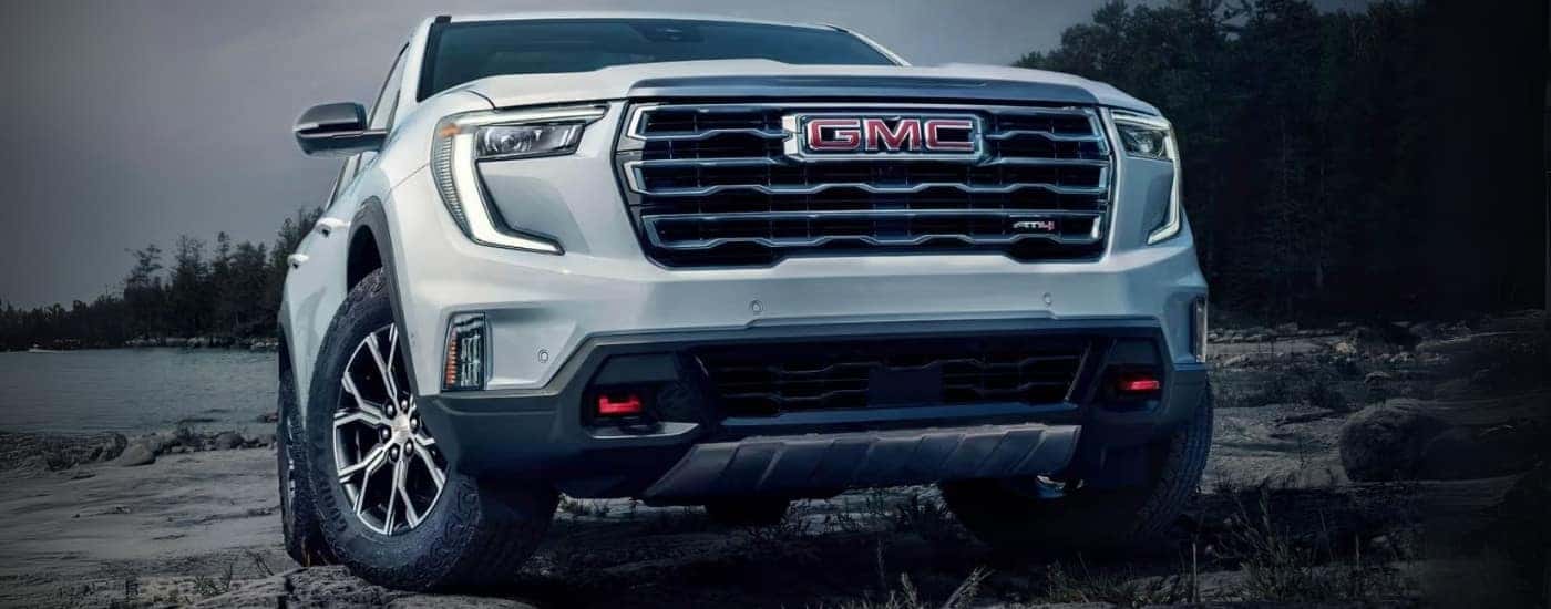 A white 2024 GMC Acadia AT4 for sale parked on rocks.