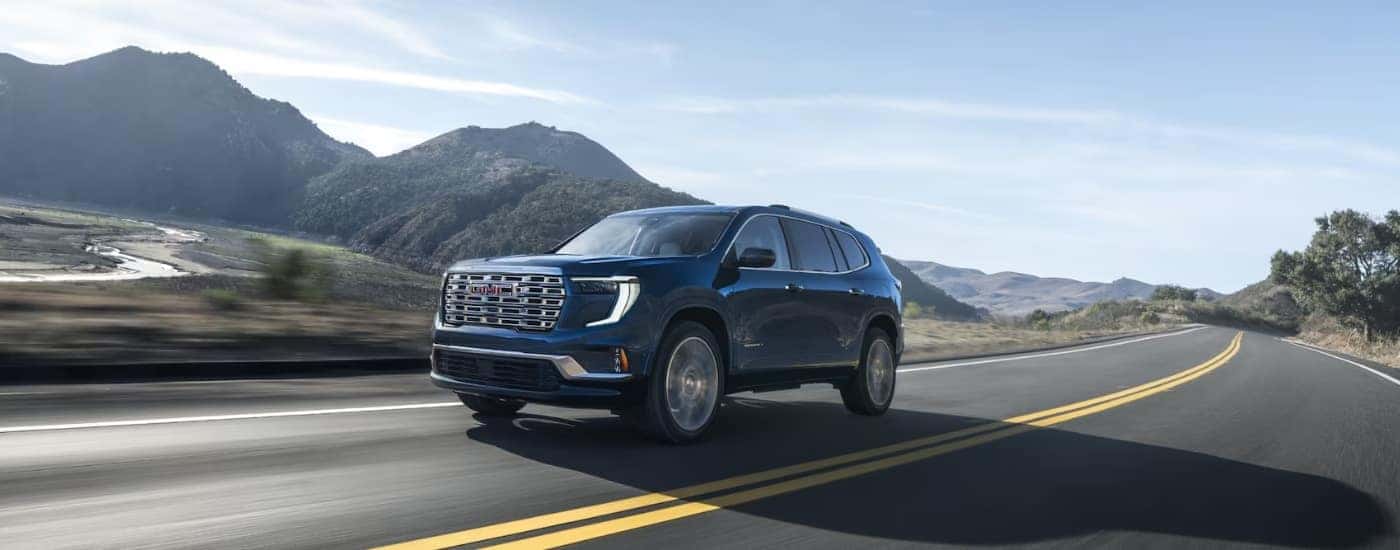 A blue 2024 GMC Acadia Denali is shown driving after viewing a GMC Acadia for sale near Aurora.