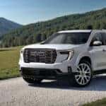 White 2026 GMC Acadia Denali Ultimate for sale near Elgin driving up a road.