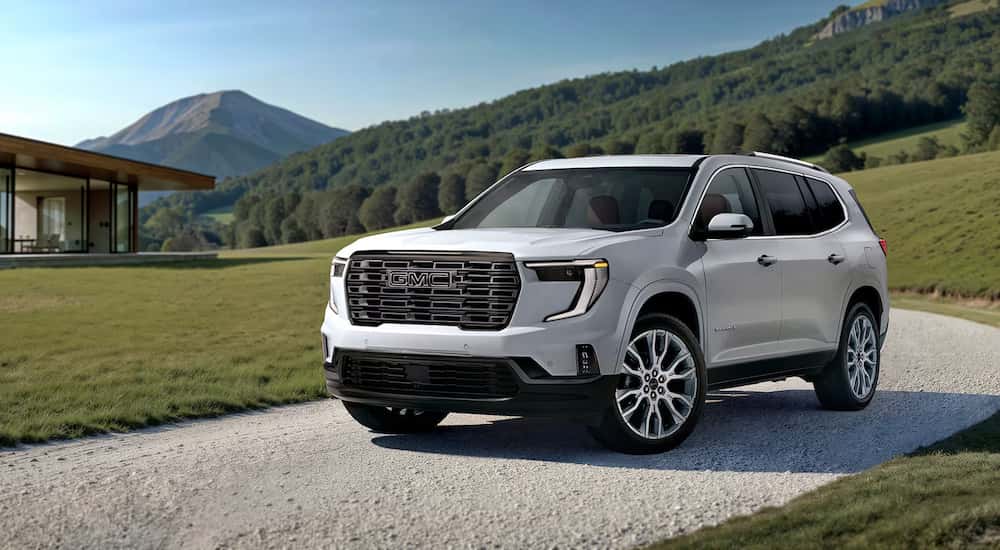 White 2026 GMC Acadia Denali Ultimate for sale near Elgin driving up a road. 