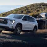White 2026 GMC Acadia towing a camper off-road.
