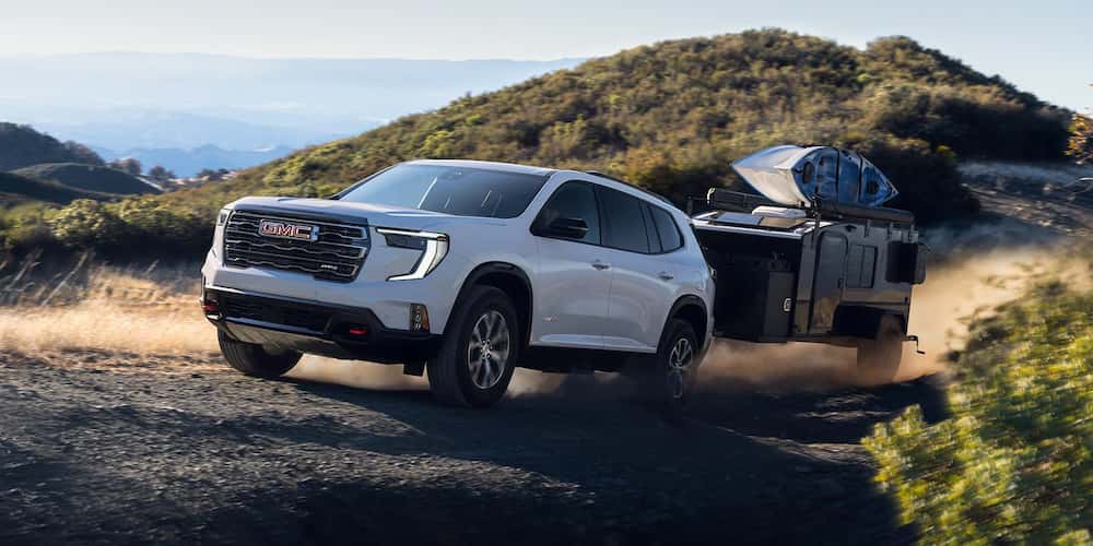 White 2026 GMC Acadia towing a camper off-road.