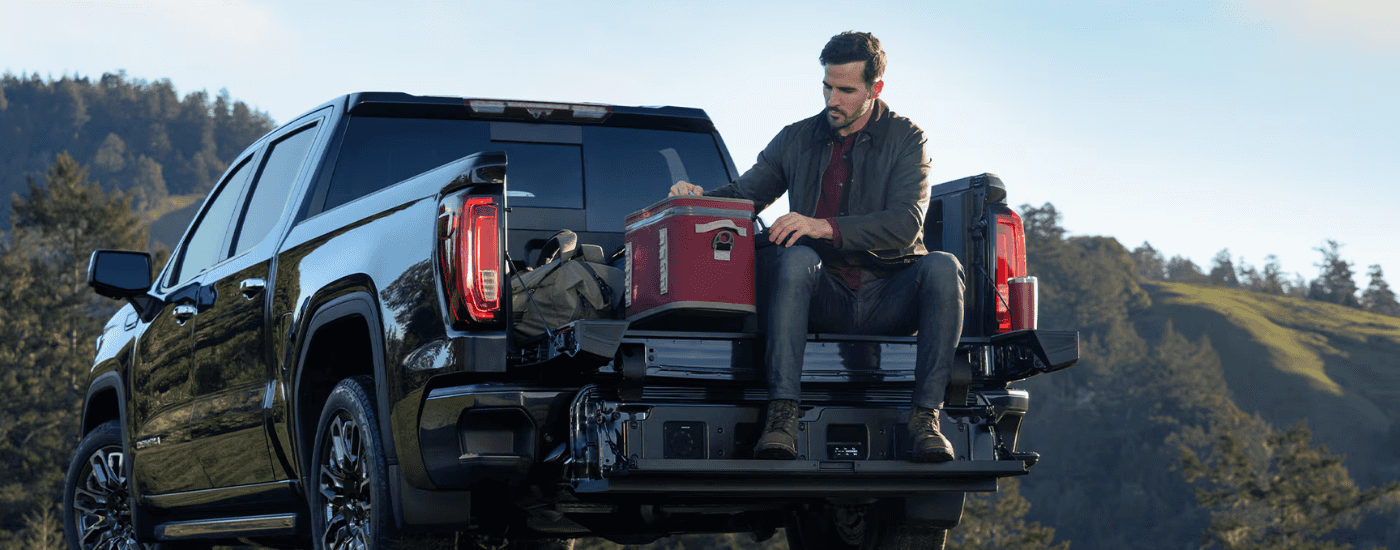 A person sitting on the tailgate of their black 2026 GMC Sierra 1500
