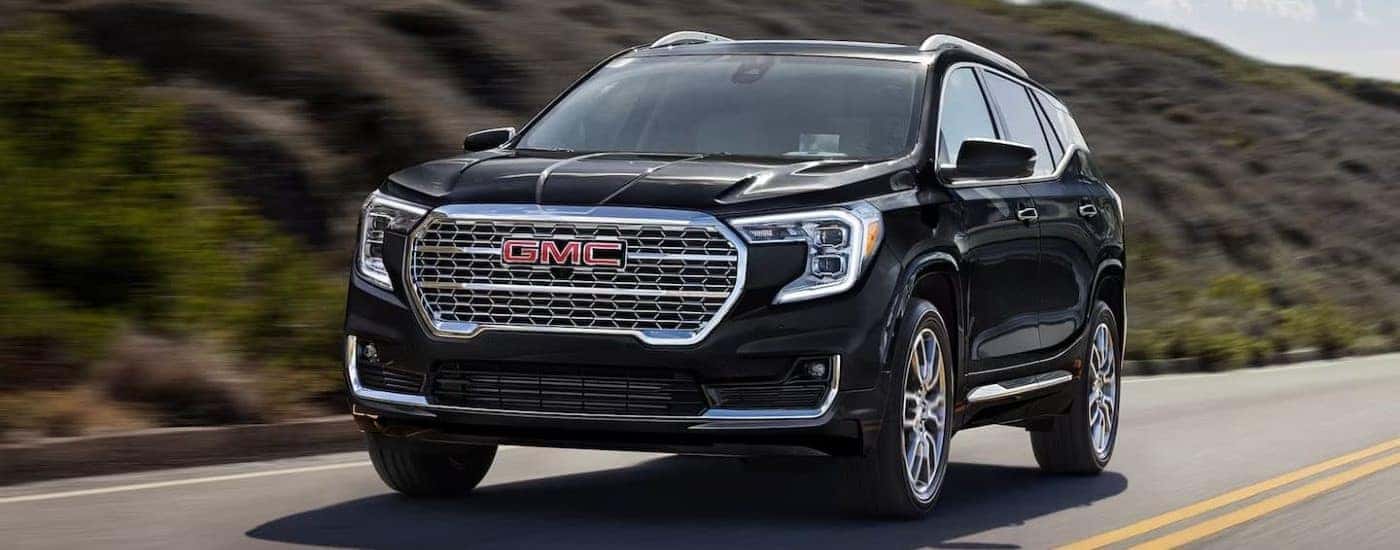 A black 2024 GMC Terrain Denali shown driving past a grassy hill.