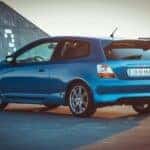 blue honda hatchback parked outside in front of garage