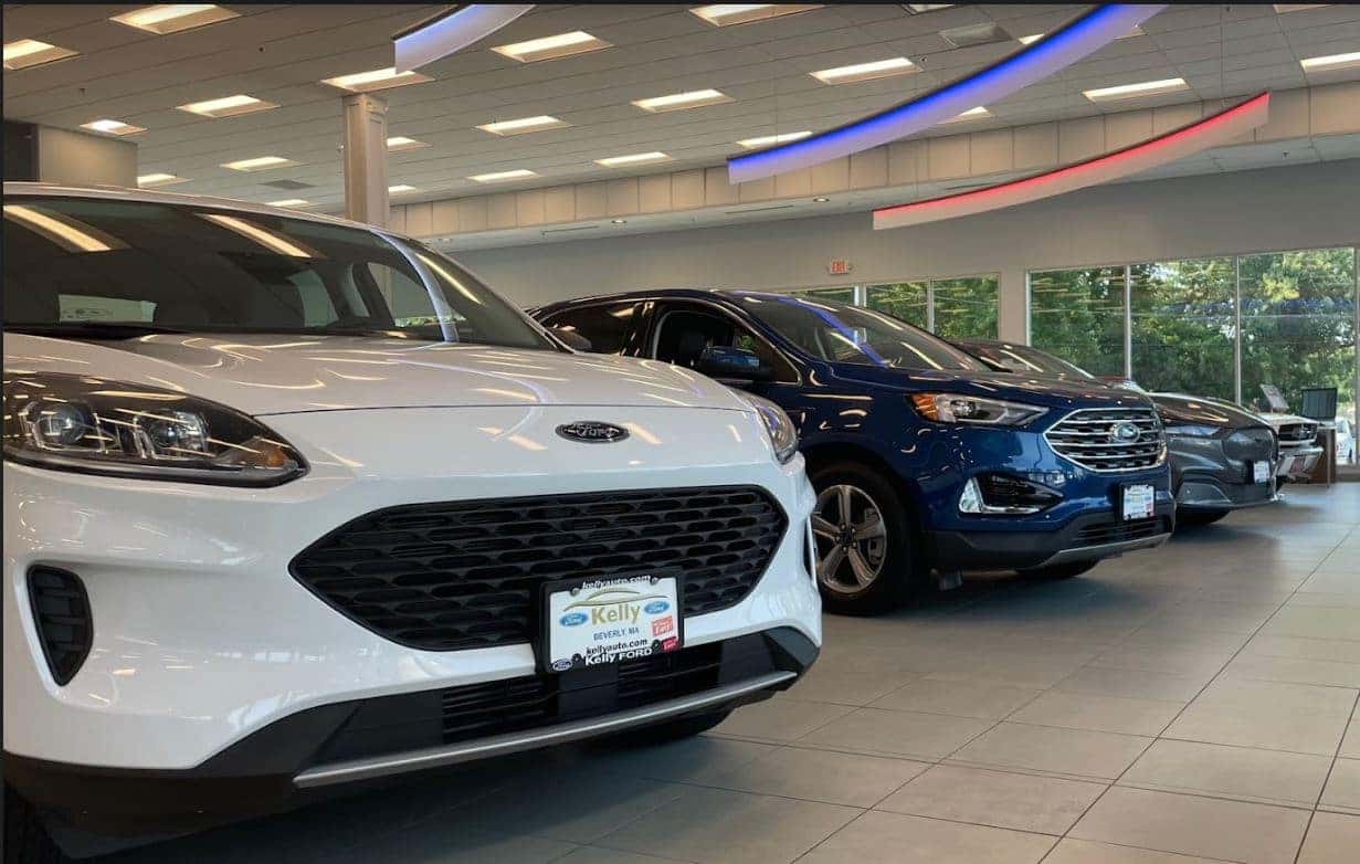 A white Ford Escape in front of Ford Edge and Ford Mustang Mach E at Kelly Ford showroom