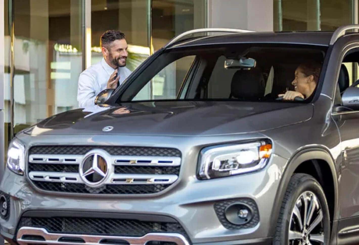 Mercedes-Benz GLB positions an advisor greeting a driver in a service center driveway.