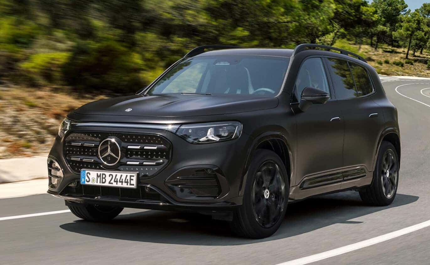 Front three-quarter view of a black 2027 Mercedes-Benz Electric GLB SUV on a tree-lined road.