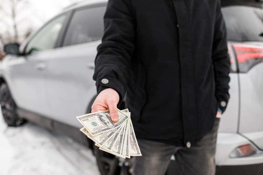 Person holding cash in front of a car