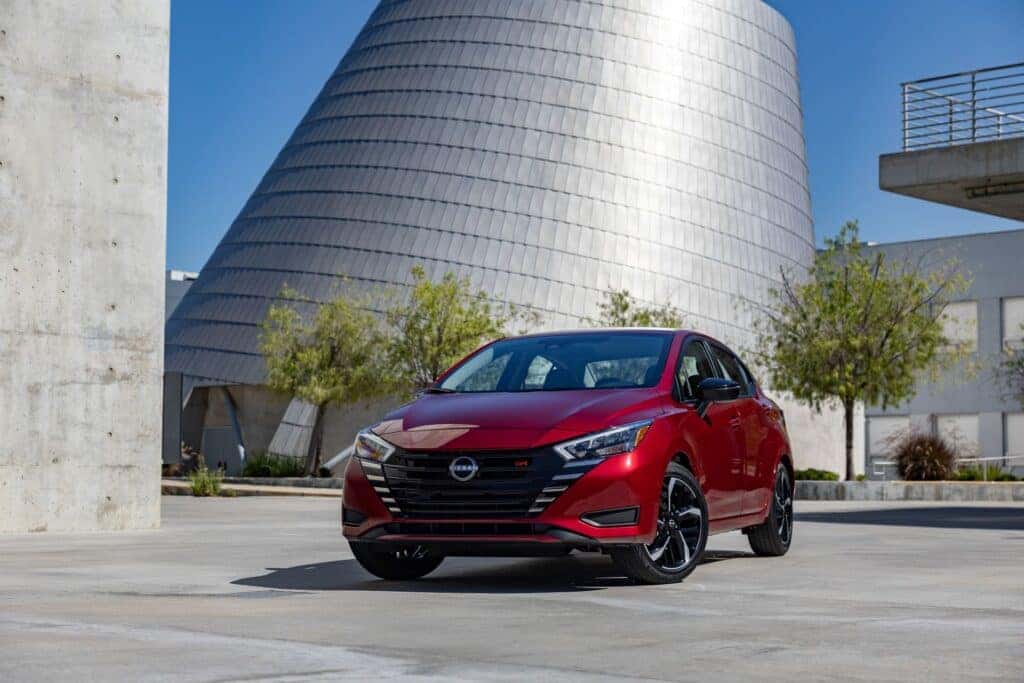 An Affordable Red 2025 Nissan Versa Parked In Front Of A Shiny Building