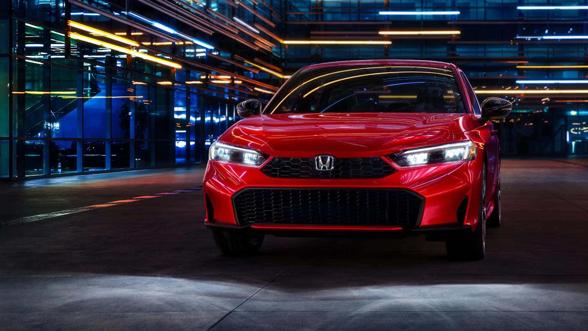 the front of a red honda civic parked at night in a warehouse full of lights
