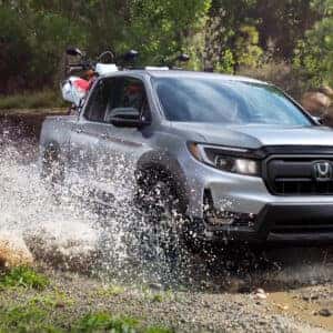 a honda ridgeline truck haulig dirt bikes going through a creekbed that is full of water and mud