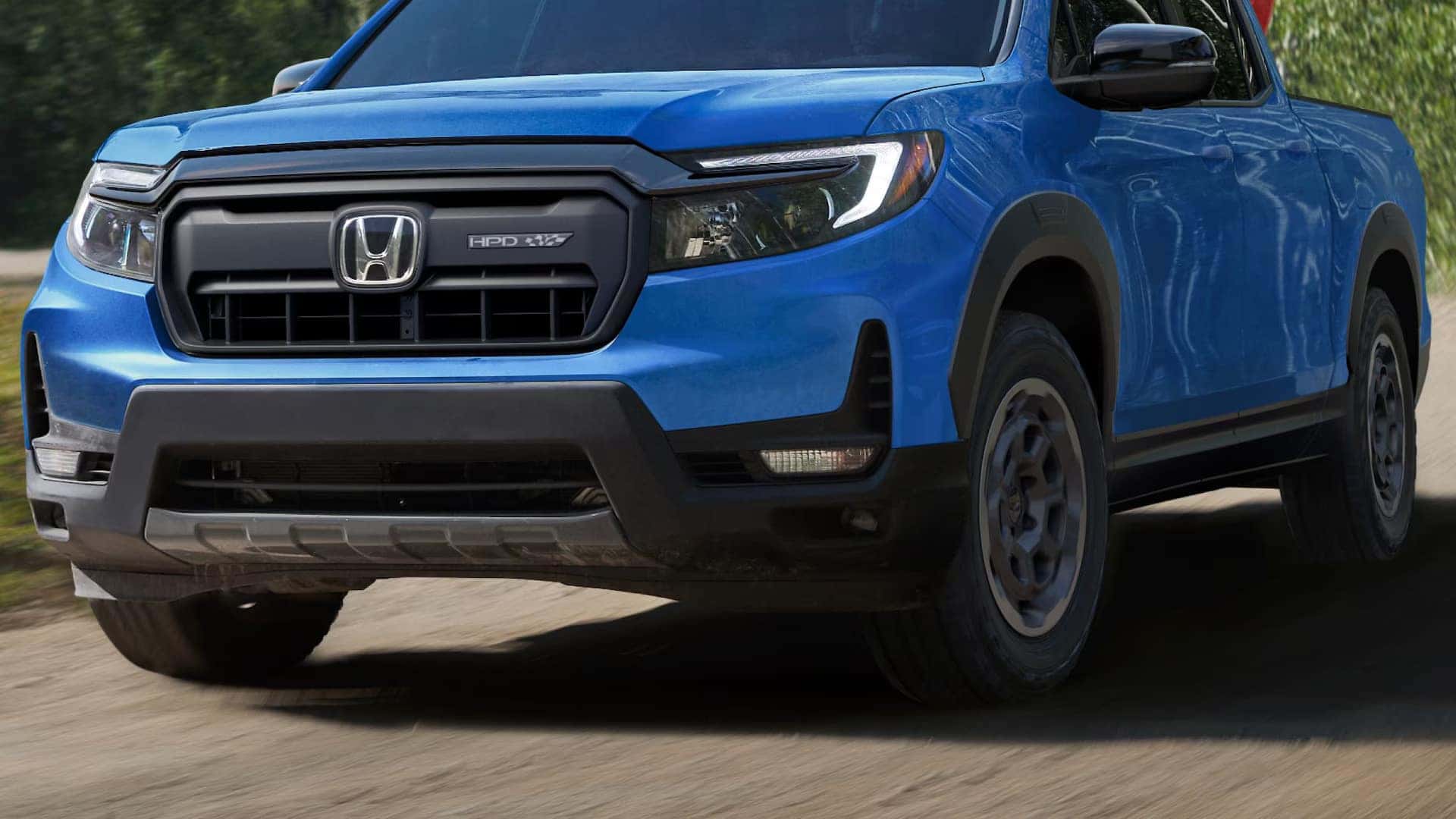 a blue honda ridgeline showcasing the tires driving on a dirt road