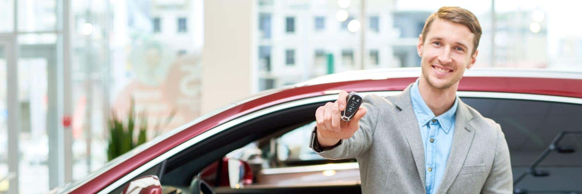 Smiling man holding a key in front of a red car