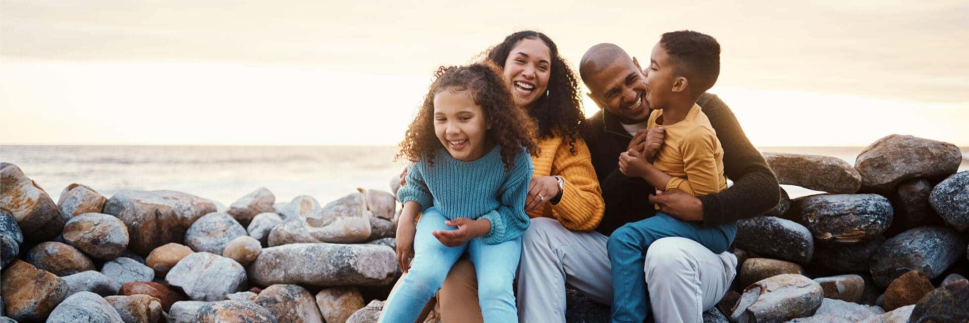 family of four smiling and sitting on rocks at the beach