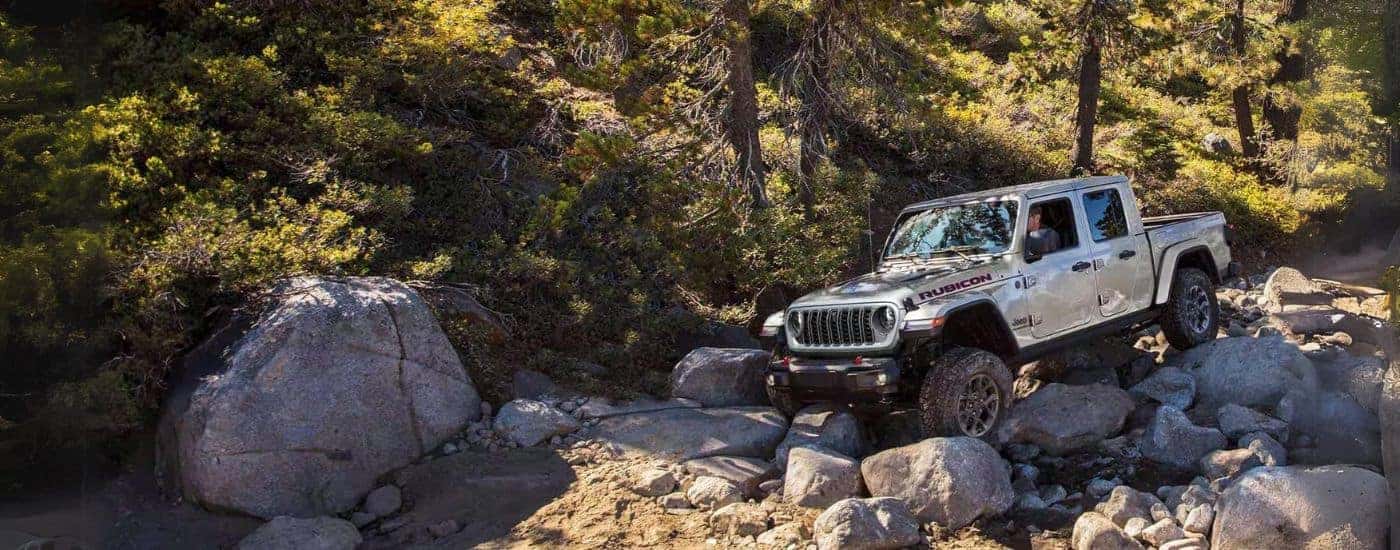 A white 2024 Jeep Gladiator Rubicon off-roading over rocky terrain. 