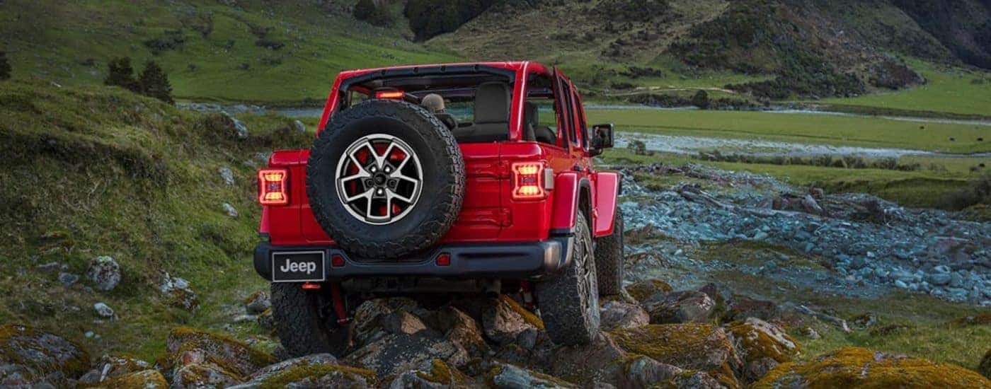 Rear view of a red 2025 Jeep Wrangler Unlimited driving away from a Jeep dealer.