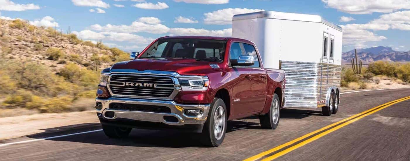 A red 2024 Ram 1500 Laramie towing a trailer on the highway.