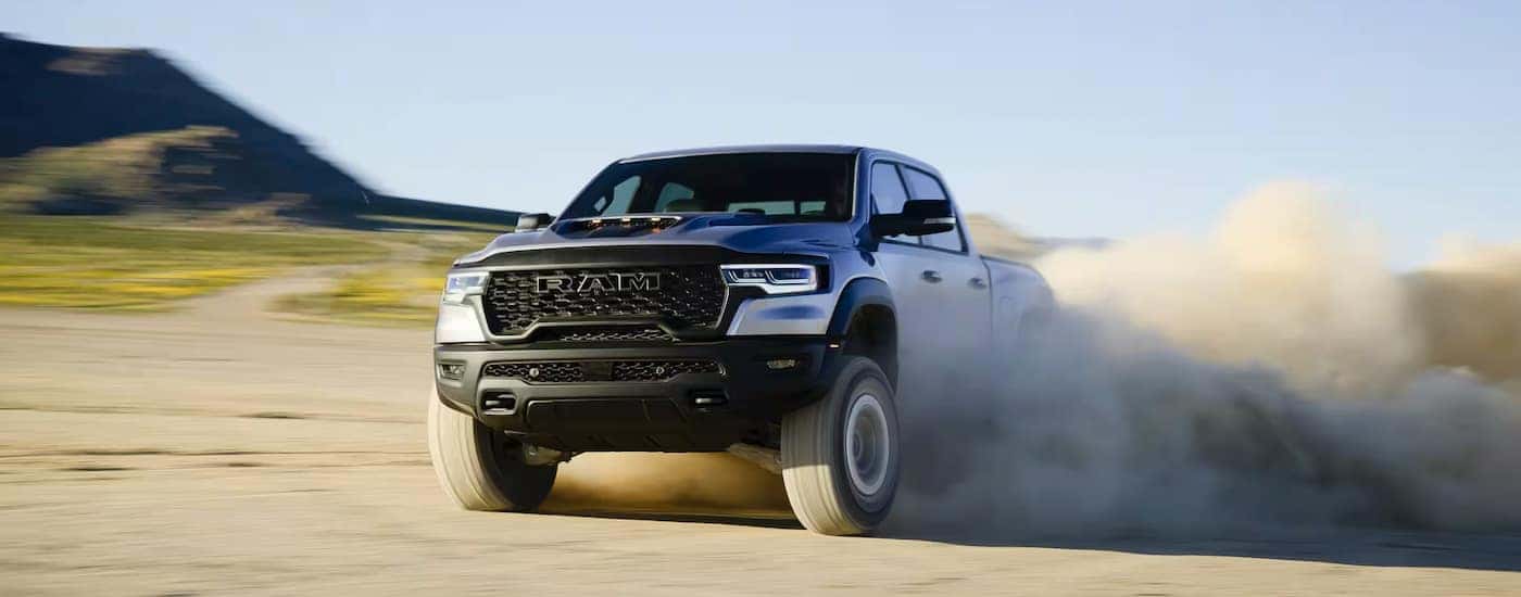 A white 2025 Ram 1500 RHO kicking up sand while off-roading.