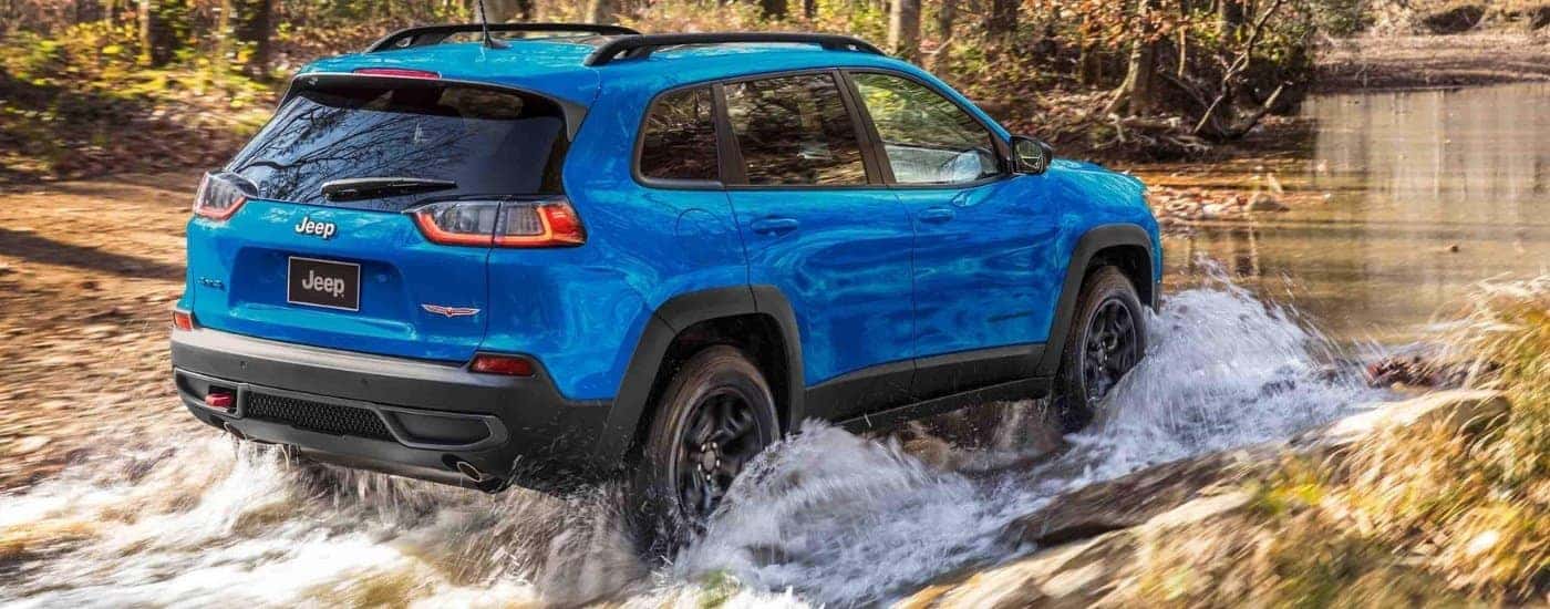 A blue  2022 Jeep Cherokee Trailhawk driving through a creek.